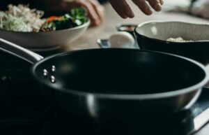 Close-up of hands preparing food with bowls and frying pan on electric stove.