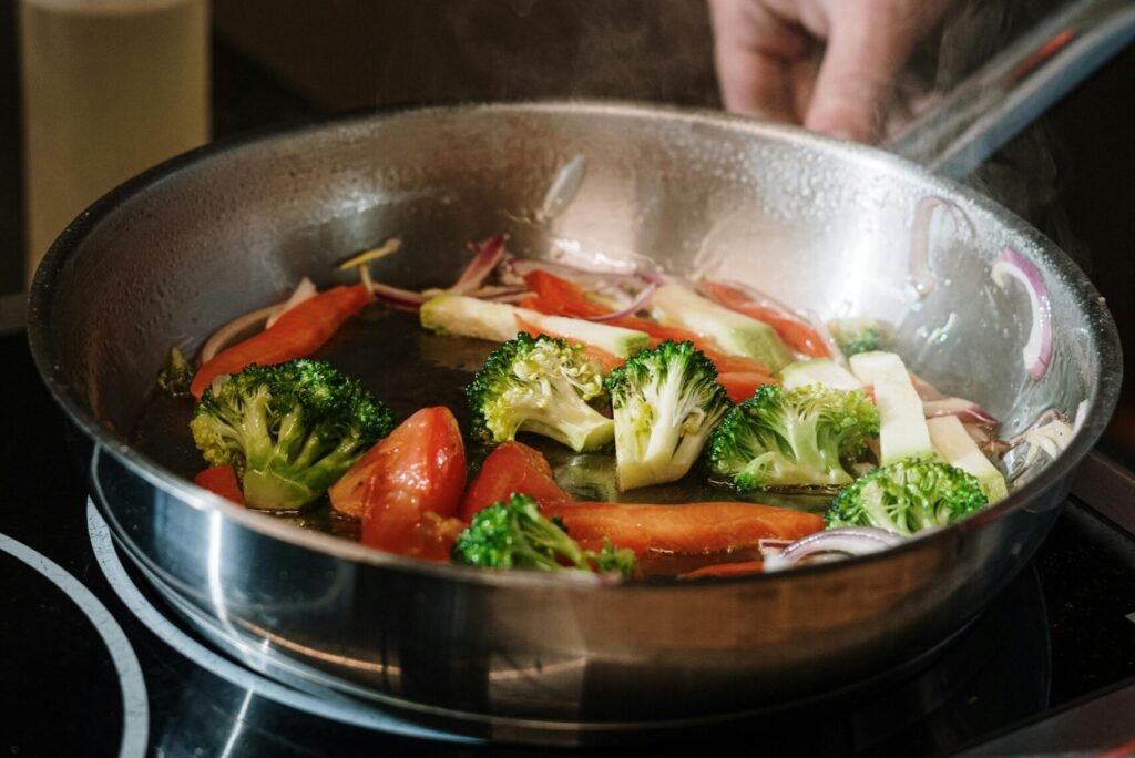 Close-up of sautéing broccoli and bell peppers in a pan on a stove.