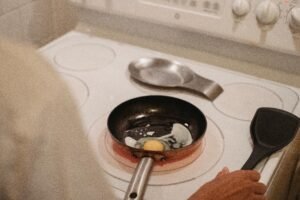 A person cooking an egg on a stovetop using a spatula, in a home kitchen setting.