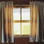 Warm sunlight streaming through fabric curtains in a wooden interior setting.